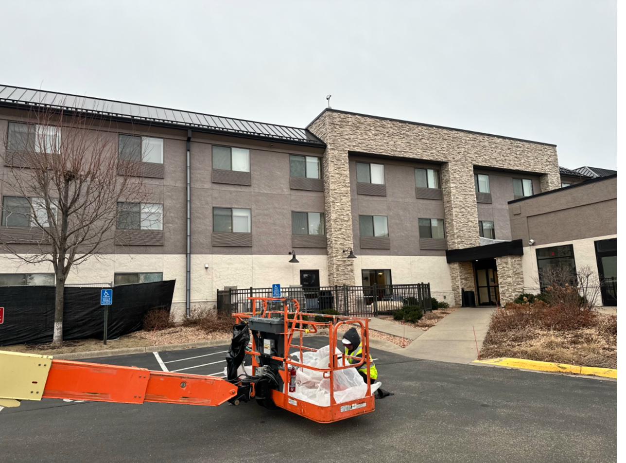 Holiday Inn Express during window installation — active job site, privacy fence, lift in place